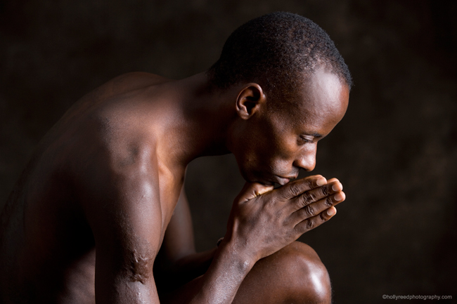 Gilbert Tuhabonye sitting down with head bent and hands clasped in front of his face