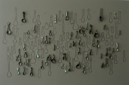 spoons of different sizes and shapes made of clay hanging on a wall interspersed with outlines of more spoons