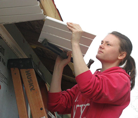 Olivia Sisk on a ladder attaching roofing