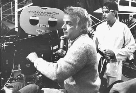 black and white image of Avildsen operating movie camera with Ralph Macchio in background