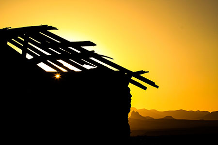 silhouette of a structure with a damaged roof against a golden sky with sunset in the background