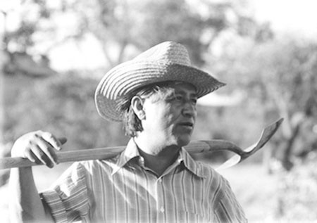 black and white photo of Chavez wearing a cowboy hat and a shovel slung over his shoulder