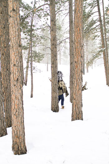 person standing next to a tree in a forest covered with snow and wearing a black and white mask