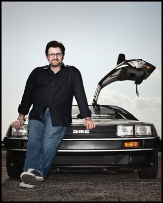 Ernest Cline sitting on his DeLorean with one door open