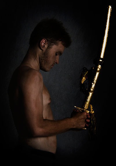 side view of a man with head bowed as if in prayer and holding a gold sword in clasped hands