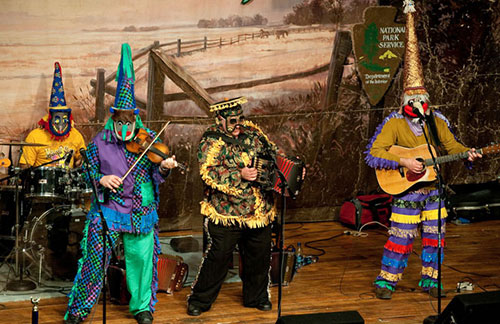band members on stage in mardi gras costumes playing guitar, accordion, violin and drums