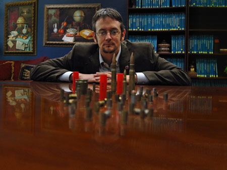 King sitting at conference table looking at a group of different bullets placed standing up on the table