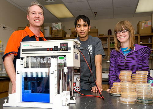 Todd Primm with two of his students standing next to research equipment