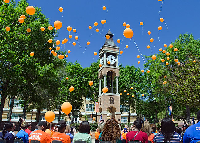students gathered around the campus clock tower releasing orange balloons