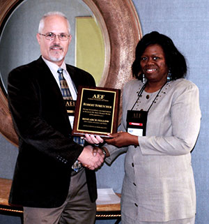 Jocelyn Evans and Robert Stretcher holding award plaque and shaking hands