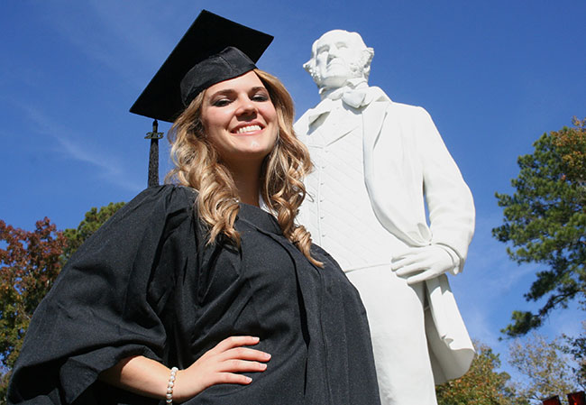 Landsman poses in graduation garb in front of Sam statue