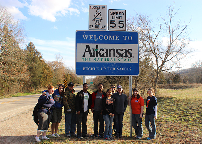 students standing at the Arkansas state line in front of the sign
