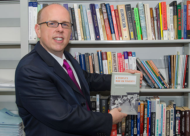 Phelps in ront of bookshelf holding his book