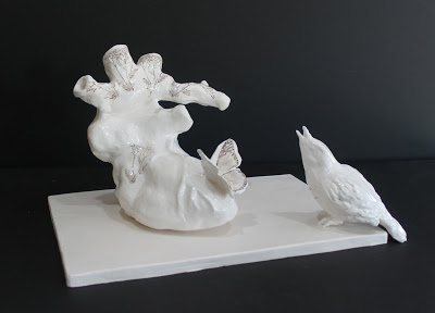 white clay sculpture with a butterfly sitting on top of an anatomical heart with a singing bird sitting next to it